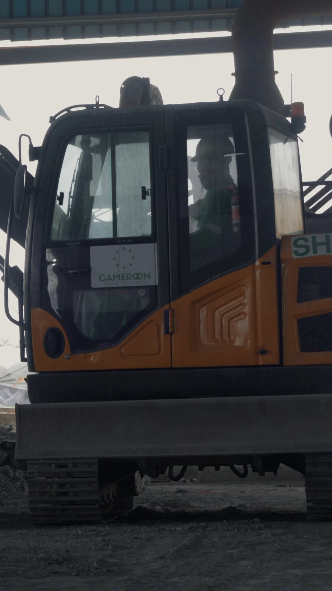 Excavator under a shed, in front of a heap of aluminium dross giving off steam