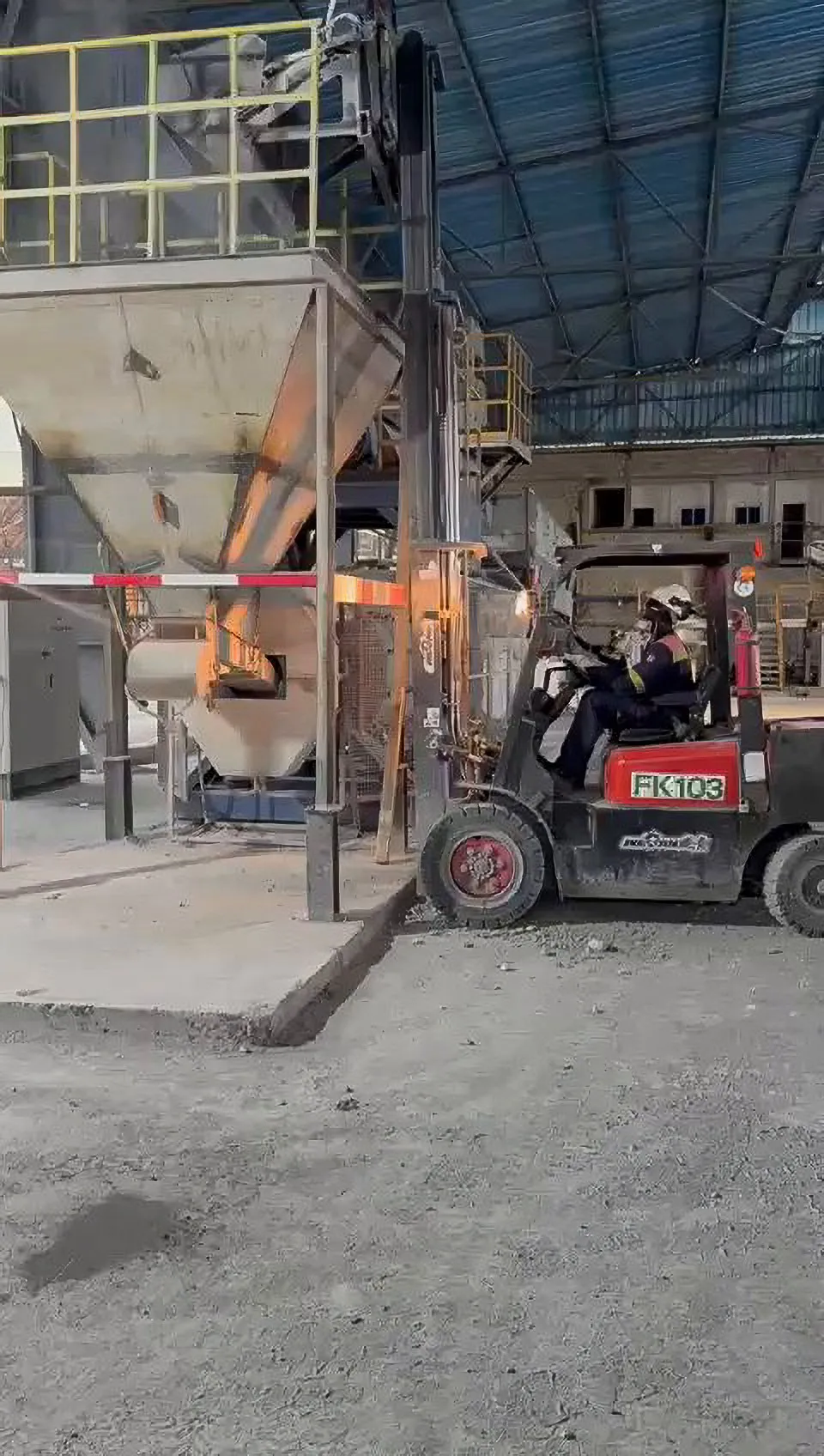 Forklift driven by an operator in a helmet, at the foot of a hopper, under a shed