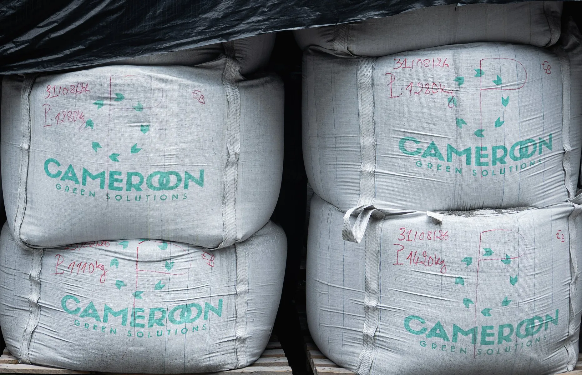 Large filled bags stacked on pallets, under a black tarpaulin