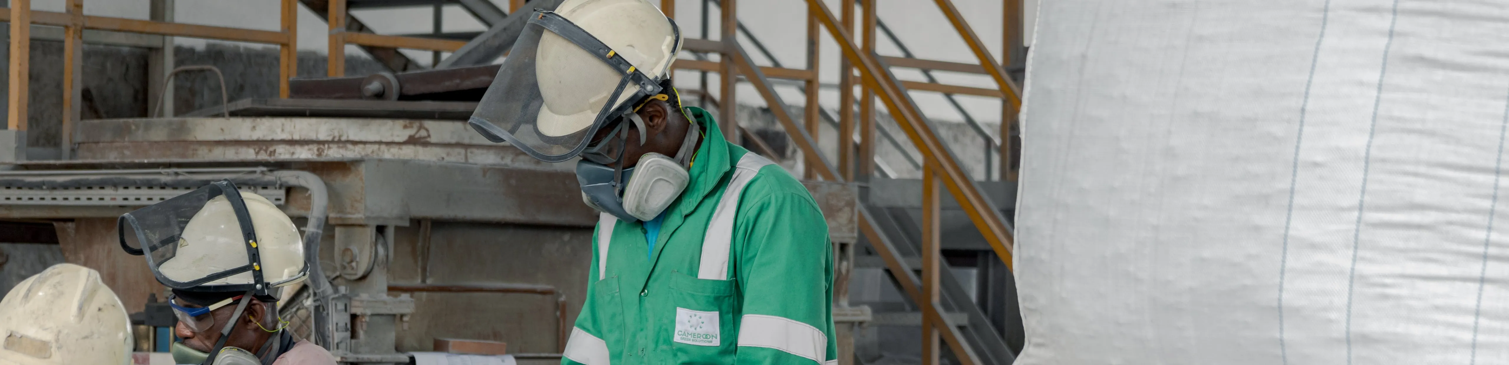 Operator in green workwear, visored helmet and respirator, at the workstation