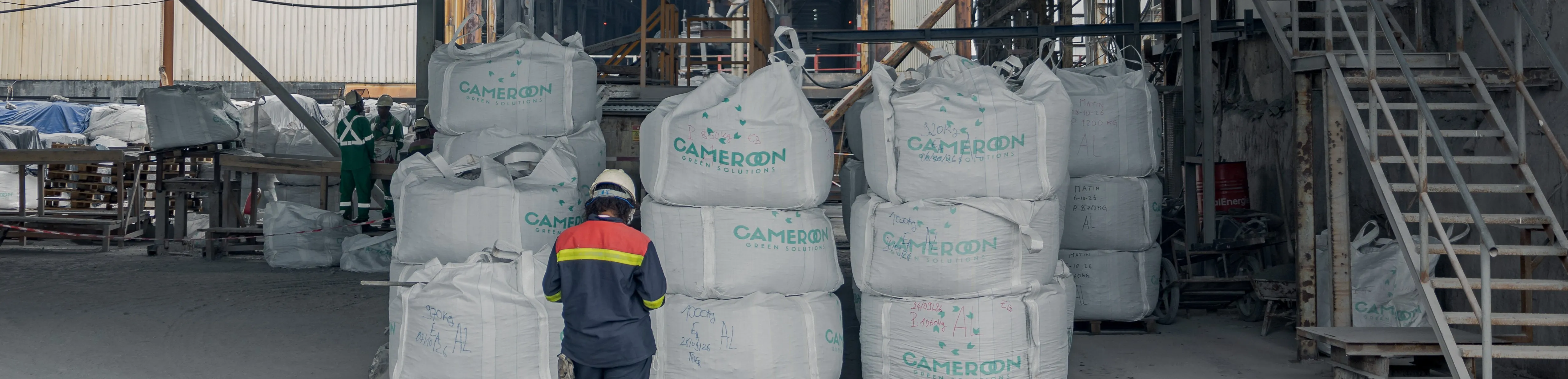Large white bags stacked in the plant hall, with an operator in a helmet seen from behind in the foreground