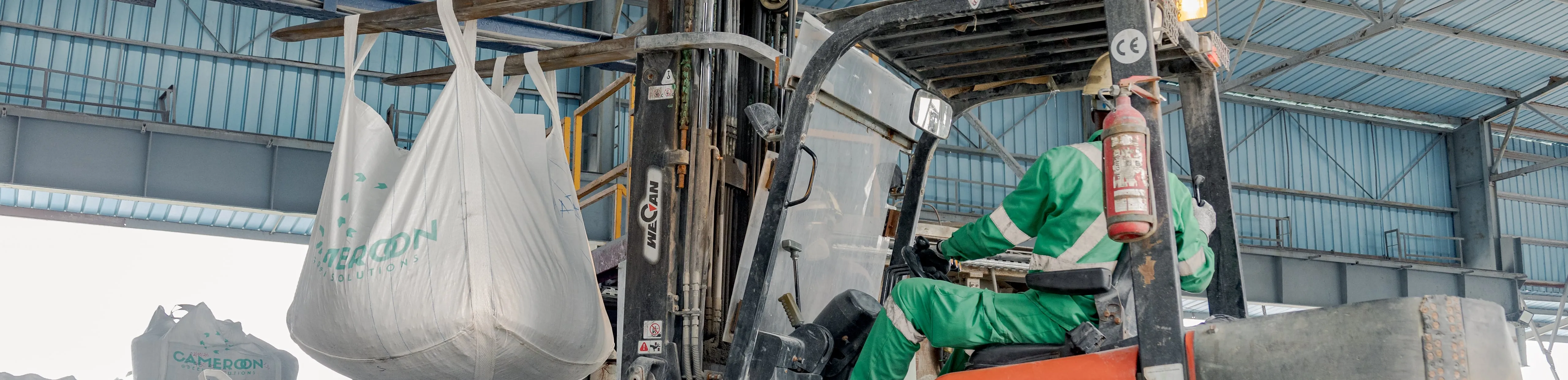 Forklift lifting a large bag, driven by an operator in green workwear