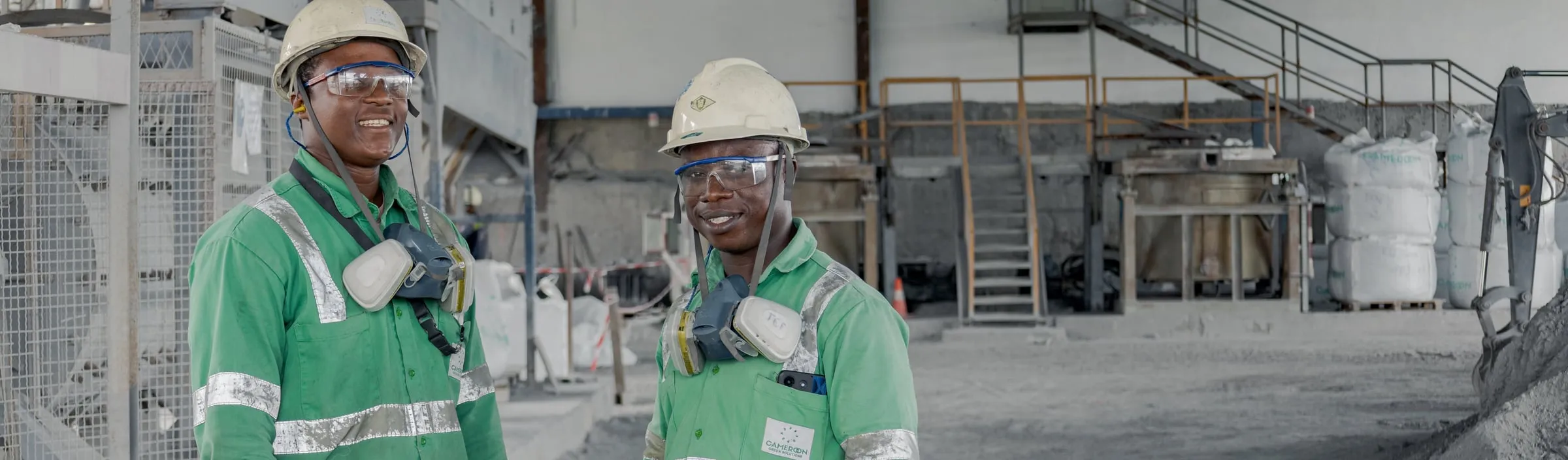 Two smiling operators in green workwear and white helmets in the workshop