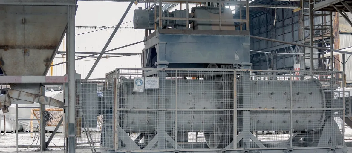 Industrial crusher behind a safety grille, under a steel roof frame