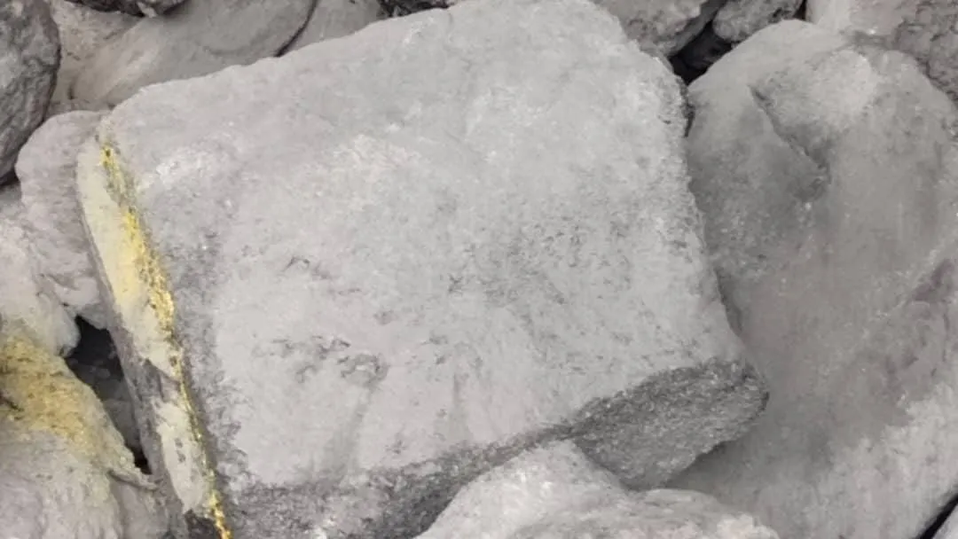 Blocs gris de cathodes carbonées entassés, un trait jaune sur le bloc central